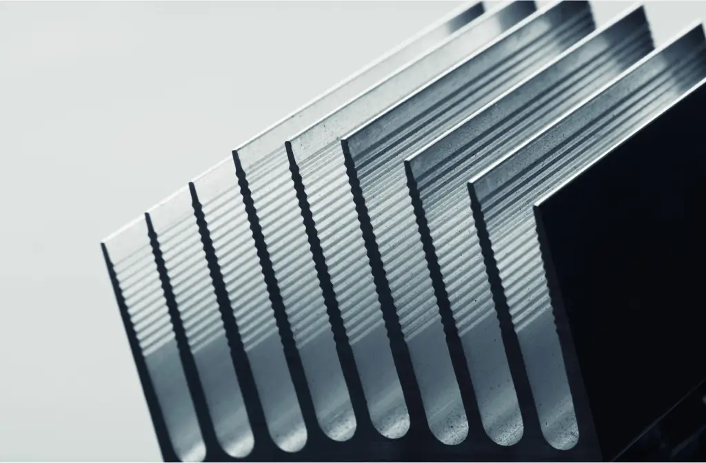 A close-up shot of silver metallic heat sink blades with evenly spaced fins, arranged in a parallel formation. The image highlights the precision and texture of the fins against a blurred background.